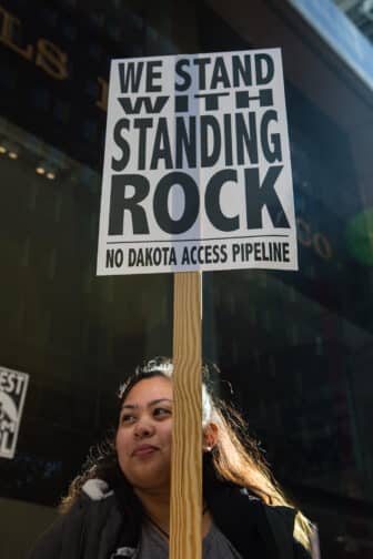 Photo of a woman holding a sign that reads: "We Stand with Standing Rock"
