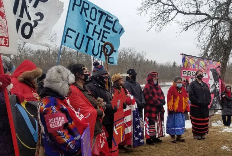 Line of Indigenous water protectors standing in a line with signs reading "protect the future"