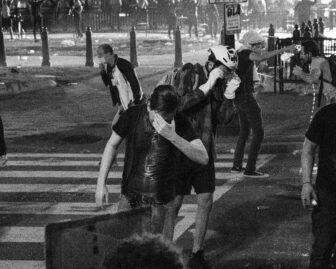 People struggling after being pepper sprayed. They are rubbing their eyes and one person pours water on another person.