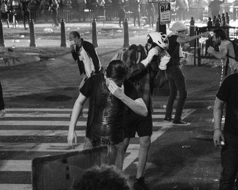 People struggling after being pepper sprayed. They are rubbing their eyes and one person pours water on another person.