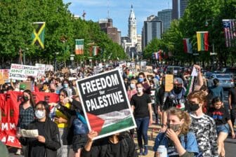Large protest for Palestinian liberation. Someone holds a sign in the front of the crowd that reads "Freedom for Palestine"