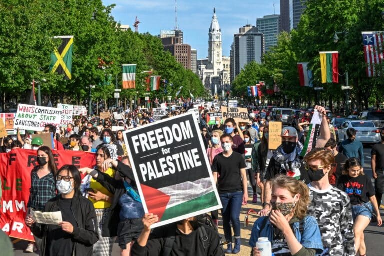 Large protest for Palestinian liberation. Someone holds a sign in the front of the crowd that reads "Freedom for Palestine"