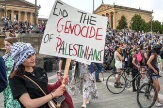 Photo of a woman in Philadelphia holding a sign at a protest that reads "End the Genocide of Palestinians"