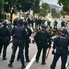 Group of police officers encircling a group of teenagers sitting on the ground.