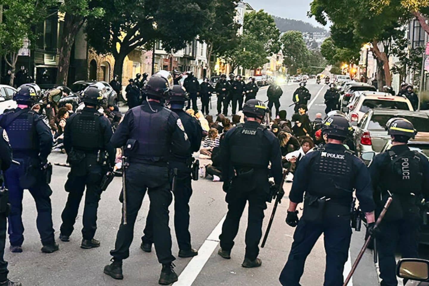 Group of police officers encircling a group of teenagers sitting on the ground.