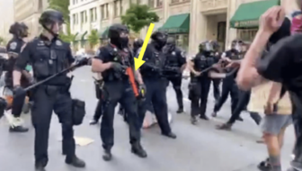 Photo of militarized police officers with an arrow pointing to the weapon that one of them is holding. The weapon is red.