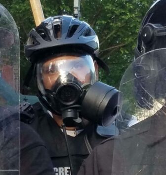 Photo of a cop in riot gear with a respirator mask on and eye shield.