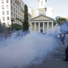 Photo of police and a cloud of what looks like smoke. You can also see protestors in the back.