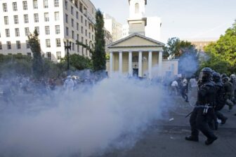 Photo of police and a cloud of what looks like smoke. You can also see protestors in the back.