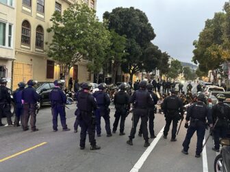 Photo of several cops encircling a group of teenagers seated in the middle of the street