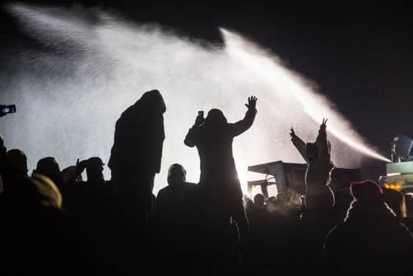 Backlit photo of people being sprayed with a water cannon at Standing Rock