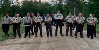 Line of police officers standing blocking a dirt road.