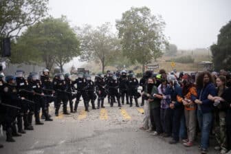 A wall of police officers standing in front of a group of people linking arms.