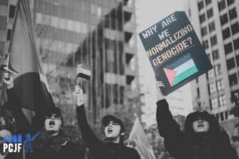 Photo of three women protesting, one holds a Palestinian flag and another holds a sign reading "Why are we normalizing genocide?"